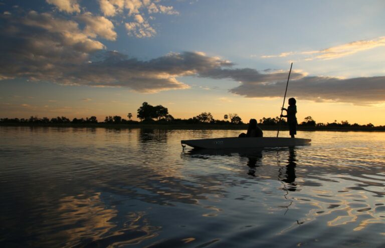 Personen in een mokoro op een rivier bij zonsondergang