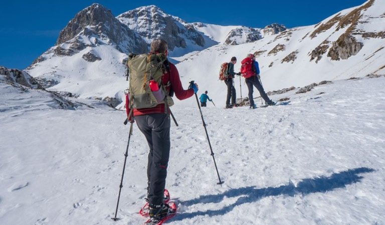 Een trail groep klimt een besneeuwde berg op onder een blauwe lucht