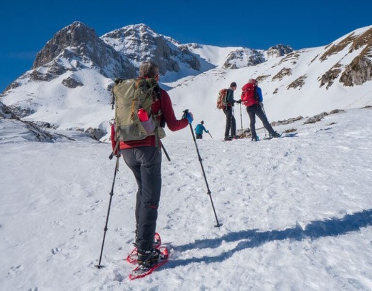 Een trail groep klimt een besneeuwde berg op onder een blauwe lucht