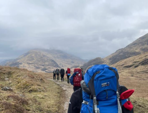 Wandelaars met rugzakken op een bergpad onder een bewolkte lucht