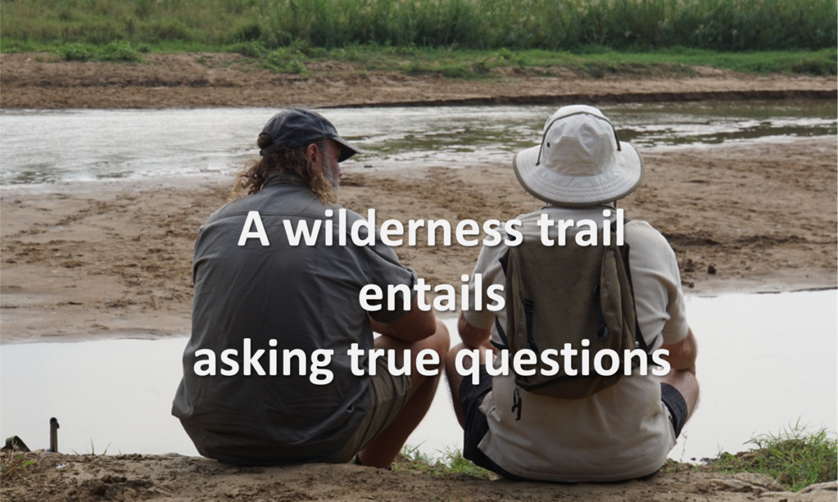 Twee mannen zitten bij een rivier met de tekst 'A wilderness trail entails asking true questions'